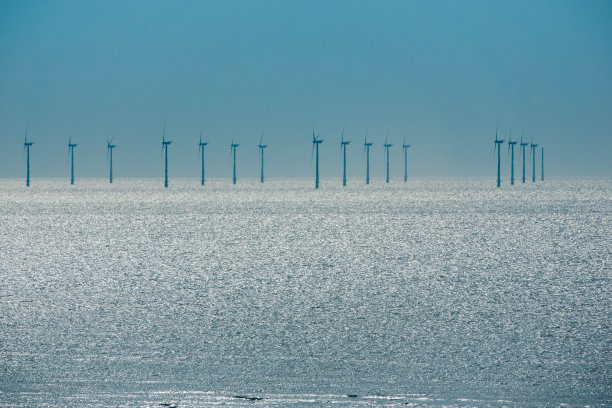 现代风力涡轮机一排排地矗立在海上。太阳在水面上的倒影图片下载