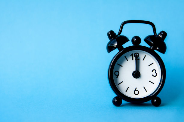 黑色闹钟隔离在蓝色背景上。时钟定在中午12点。复制时空概念图片下载