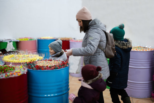 快乐的小孩子和妈妈在糖果店挑选糖果，果酱糖果，把它们放在纸袋里。图片下载