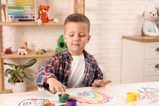 小男孩在室内白色的桌子上用手指画画图片下载