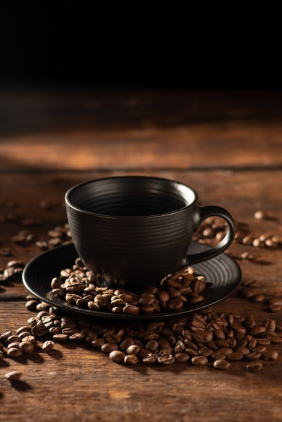 黑色的杯子，黑色的杯子旁边有咖啡豆在质朴的木头上，深色的食物风格的照片，选择性的聚焦。图片下载