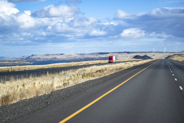 景观与红色大钻机半卡车与干货车半挂车行驶在分割的高速公路上，电动风力涡轮机的背景图片下载
