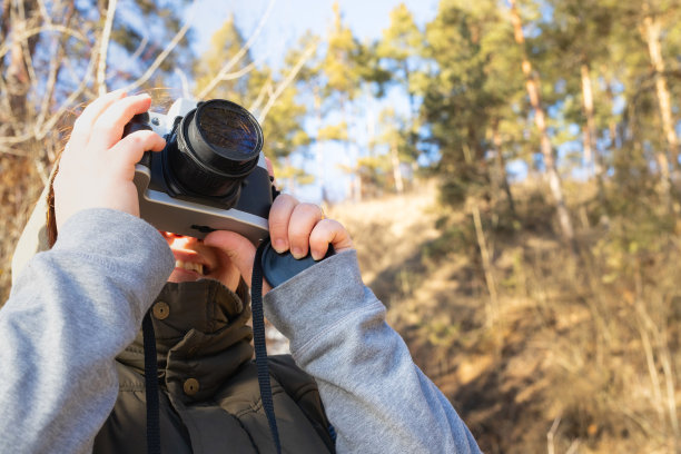 女摄影师在户外拿着相机靠近她的脸，微笑着享受大自然的照片，一个美好的冬日阳光明媚的日子。图片下载