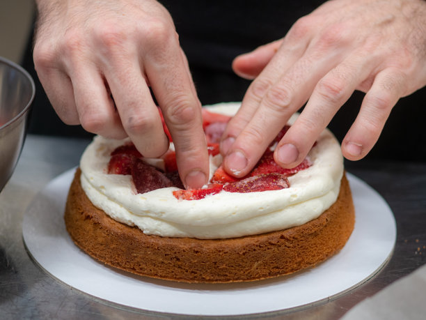 糕点设计师厨师制作了一个三层蛋糕，里面有草莓和奶油奶油图片下载
