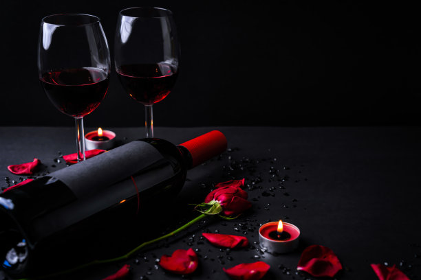 情人节:一瓶红酒，眼镜，蜡烛，红玫瑰，心形盒子和黑色背景图片下载