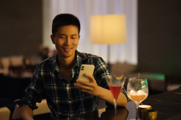 微笑的亚洲年轻男子看着手机在酒吧图片下载