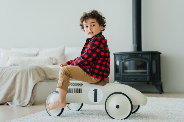 Curly caucasian little boy in plaid shirt and casual pants sitting on toy car at bedroom looks at camera. Handsome child received a present from parents. Cute toddler playing at home. Childhood. â one图片下载