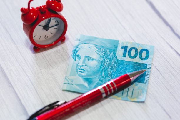 一张近距离照片中，一张价值100雷亚尔的巴西雷亚尔钞票放在一张木桌上。作文中有一支钢笔和一个闹钟。经济、投资和通货膨胀。图片下载