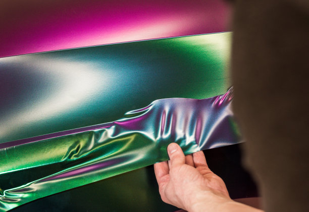 在工作过程中用变色龙色乙烯薄膜包裹汽车的专家。汽车包装专家用乙烯薄膜覆盖汽车。图片下载