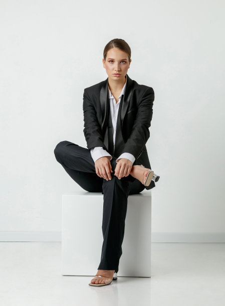 美丽的年轻女子在黑色长裤套装和白色纽扣衬衫坐着，看着相机图片下载