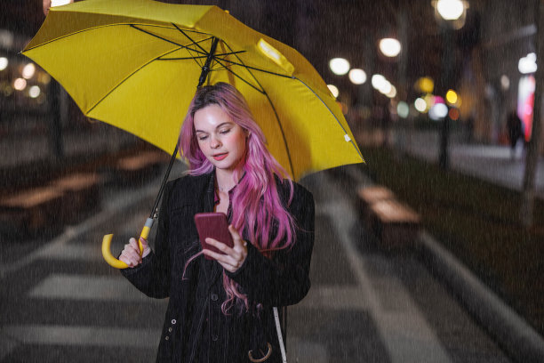 雨夜，一位年轻女子打着黄色的雨伞走在街上，一边打着电话。图片下载