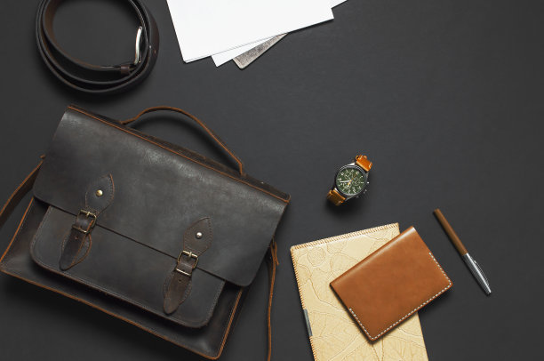 时尚的概念。棕色皮革男士包，手表，皮革护照封面，钢笔，空白的白色表在黑色背景顶部视图平铺与复制空间。配饰商人时尚服装图片下载