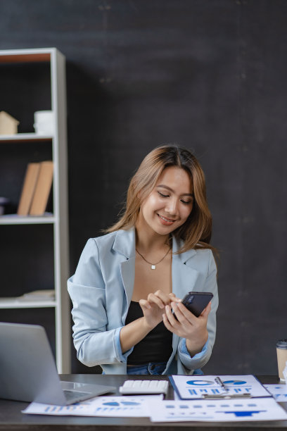 快乐的亚洲女性员工在现代大型办公公司工作经理专业商人或员工使用笔记本电脑打电话。垂直的图像图片下载