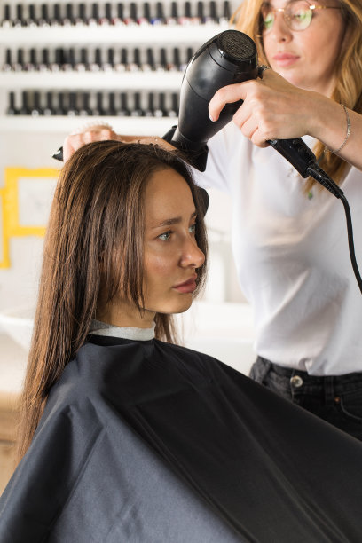 美发师用吹风机吹干客户的头发，用梳子为她的头发做造型。图片下载