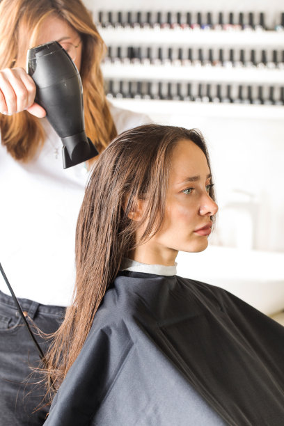 美发师用吹风机吹干客户的头发，用梳子为她的头发做造型。图片下载