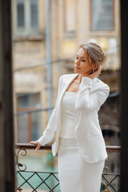 一个穿着白色西装的美丽自信的女人站在老建筑的阳台上。图片下载