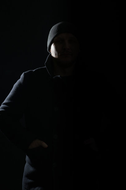 穿着外套和帽子的男人隐藏在阴影和剪影中，被光照亮图片下载