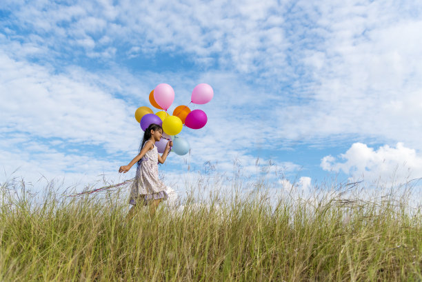 快乐可爱的女孩拿着气球在绿色的草地上奔跑，白云和蓝天与幸福。手握生机勃勃的气球玩生日派对快乐时光夏日阳光户外图片下载
