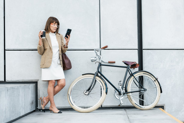 商务女性，电话和咖啡，自行车是生态友好的交通工具，可以在城市旅行时使用5g网络在线。企业家在休息时使用移动应用程序进行交流和网络图片下载