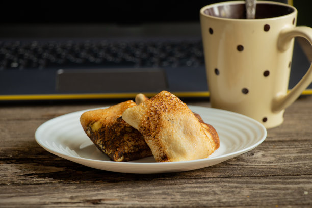 早餐是盘子里的豆腐煎饼，一杯茶和一台笔记本电脑放在家里的木桌上图片下载