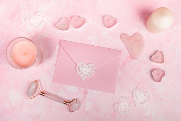 天然粉色石英石刮砂刮痧和滚筒按摩器用于面部、信封、蜡烛上的粉色。图片下载