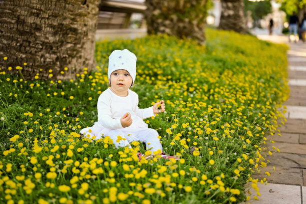 在意大利，一个快乐的小女孩坐在外面有黄花的草地上。图片下载