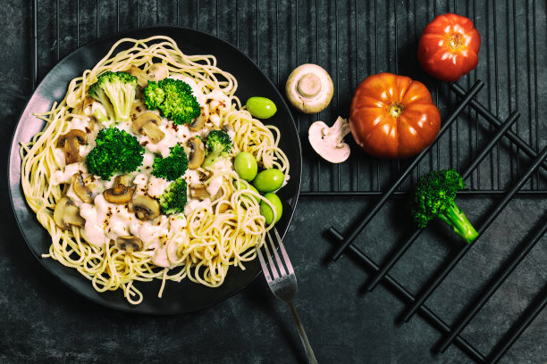 传统美味的意大利面食，鸡肉，蘑菇，西兰花，奶油酱和绿橄榄，黑色盘子，黑色背景。特写镜头。黑暗的低调照片。平面组合。图片下载