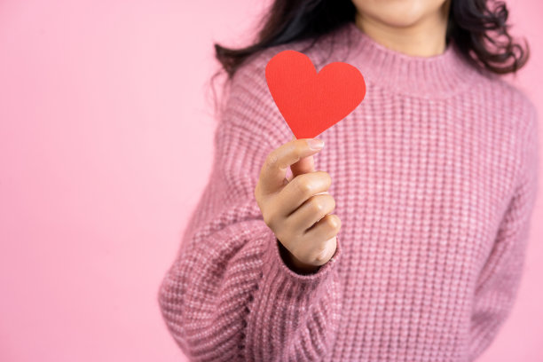 特写镜头的女性手，美丽的亚洲女人穿着粉红色的毛衣是抱着红色的爱的心孤立地站在粉红色的背景，爱的概念图片下载