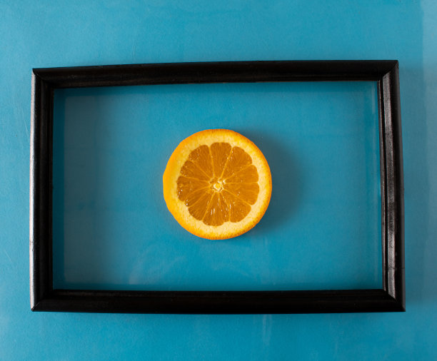 蓝色的墙上挂着一幅抽象画，黑色画框里装着一个橙子图片下载