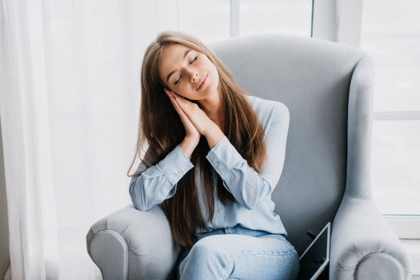 疲惫的金发白种人女子在不经意间坐在椅子上双眼合拢双手靠头劳累后远程工作，上课。美丽的意大利女孩在家里放松。睡的家庭主妇。舒适的家。图片下载