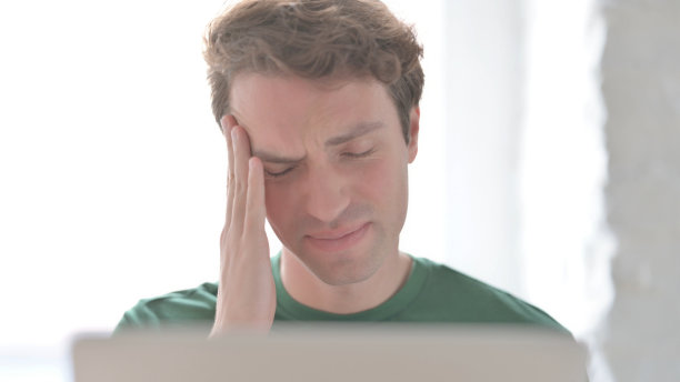 在笔记本电脑上工作时头痛的年轻人特写图片下载