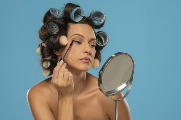 带着卷发器的女人在蓝色背景的睫毛上涂睫毛膏图片下载