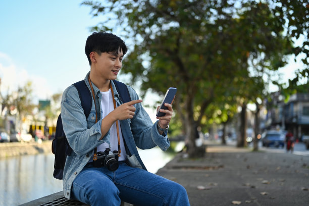 一名亚洲游客坐在河边的桥凳上用智能手机搜索方向。图片下载