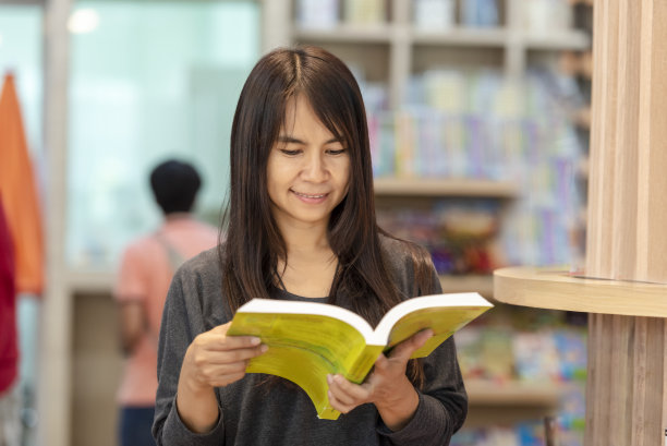 亚洲妇女在大学图书馆的书架上看书。年轻女子放松阅读开卷自学。大学女生在图书馆书店自学。教育学习知识图片下载