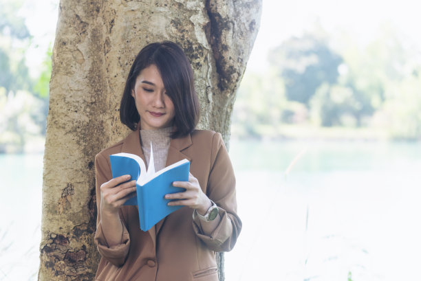 快乐的亚洲女人在绿色公园大自然的户外看书。读书杂志放松女人。休闲肖像女子微笑坐在绿色公园阅读电子书日记计划与快乐的脸图片下载