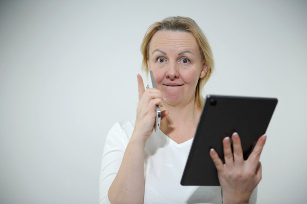 成年女子正在打电话，手里拿着平板电脑，她举起食指，露出皱巴巴的额头，惊讶地赢了，看看这里的销售很有趣，这里做衣服广告的地方图片下载