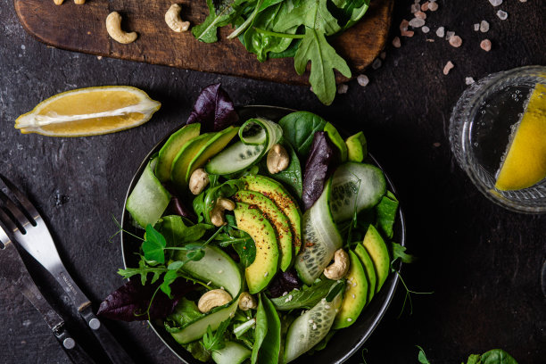 绿色蔬菜、黄瓜和牛油果沙拉放在黑暗的桌子上。素食菜图片下载