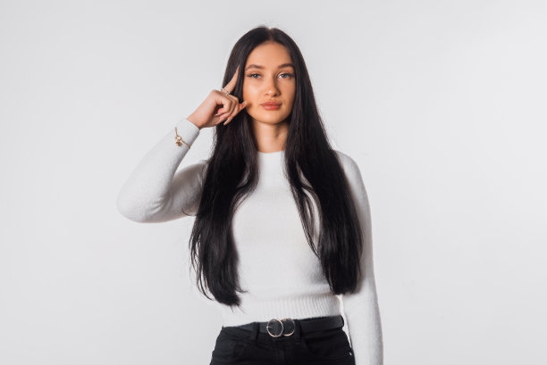 年轻认真和自信的黑发女子，看起来深思熟虑，有一个想法，站在便服白色背景。漂亮女孩想。情绪和肢体语言的概念图片下载