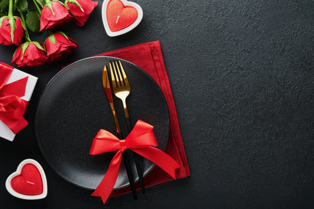 情人节浪漫的餐桌摆设。空特写红玫瑰，酒，蜡烛，晚餐黑色盘子，刀，叉和装饰丝绸心形黑色背景。节日的概念。副本的空间。俯视图图片下载