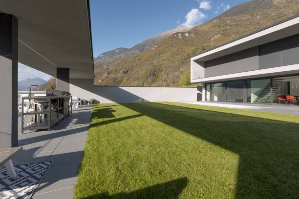 修剪整齐的花园，群山环绕的现代别墅。阳光灿烂的日子图片下载