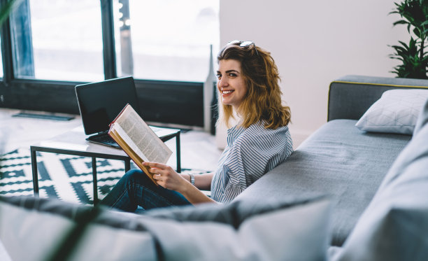 开朗的白人潮女孩休息与文学爱好感觉放松在舒适的公寓地板上坐着上网本做e学习，快乐的女人与畅销书微笑图片下载
