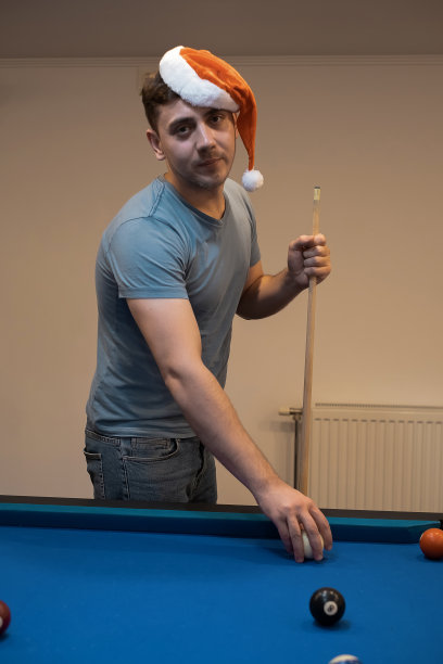一个戴着圣诞老人帽子的男人把手放在台球桌上，打斯诺克或准备打台球，端口游戏斯诺克台球，打台球图片下载