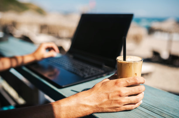 一个不认识的男人在海滩上一边工作一边喝冰沙咖啡图片下载