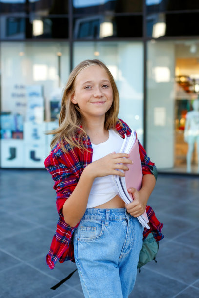 微笑的女孩站在街上，拿着笔记本。儿童户外。回到学校的概念图片下载