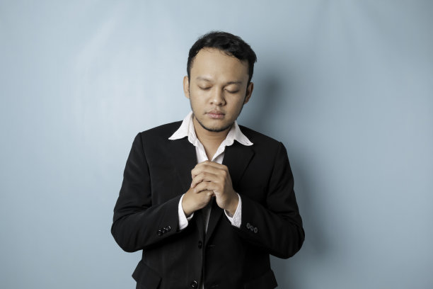 身穿黑色西装的亚洲商人的肖像被蓝色背景隔开，正在祈祷成功图片下载