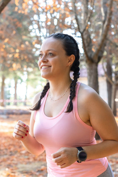 微笑运动的女人在公园里跑步。一个微笑的运动女孩在公园跑步的侧面视图。年轻的运动女子在公园里跑步图片下载