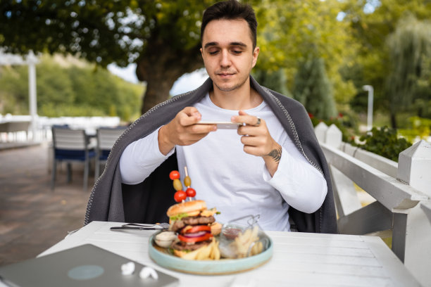 一名男子用手机拍下了桌子上盘子里的汉堡图片下载