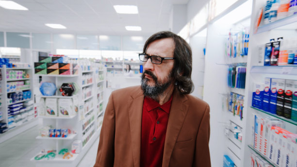 一名男子环顾药房里的药品和化妆品货架——近距离观看图片下载