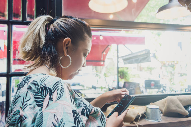 一位年轻的拉美裔妇女在餐厅门口用手机图片下载