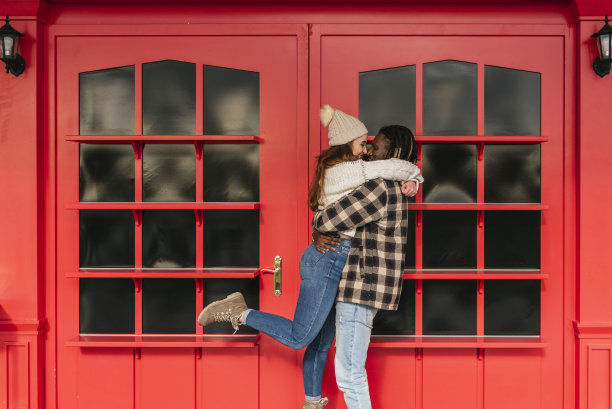 非洲裔美国男子抱起他的女朋友，背景是红色的门图片下载